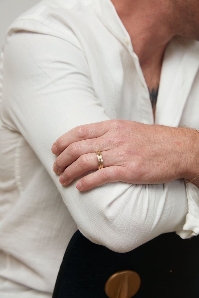 close up of man's hand wearing gold band with notched detail around center