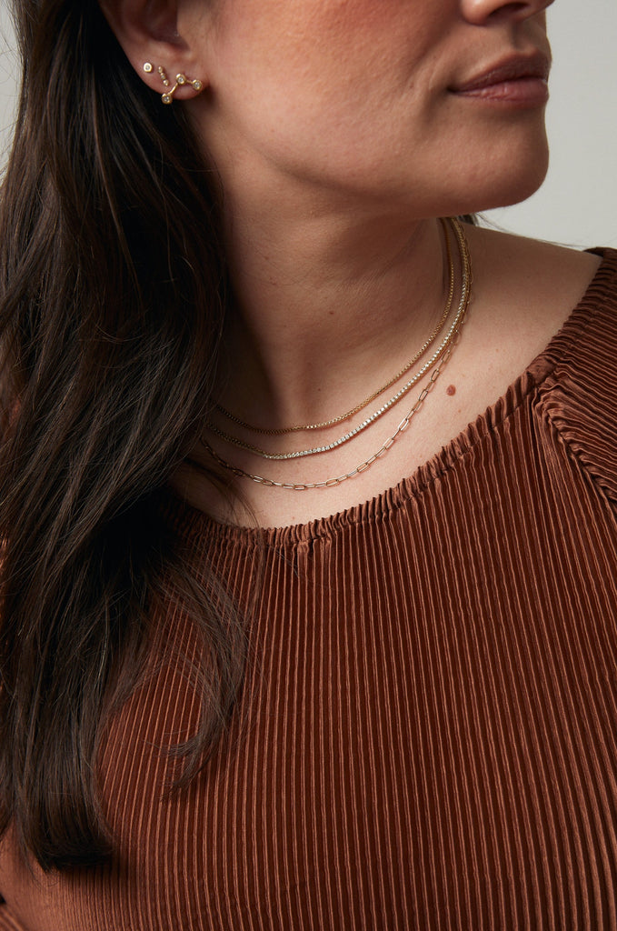 gold box chain necklace layered with diamond line necklace and cable chain necklace