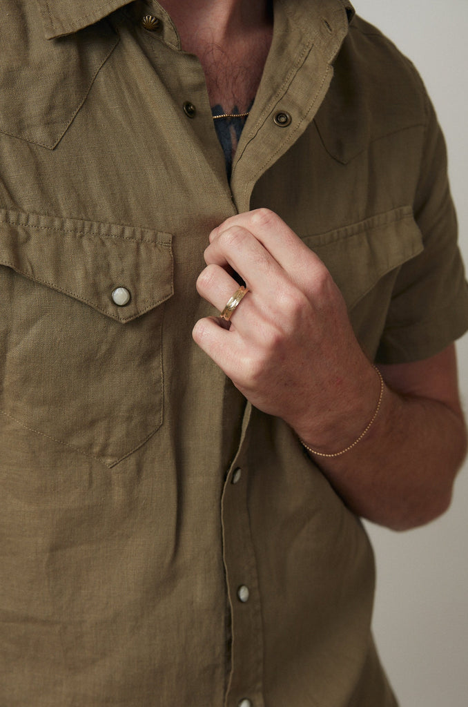 close up of man's hand wearing gold band with notched detail around center alongside other gold jewelry