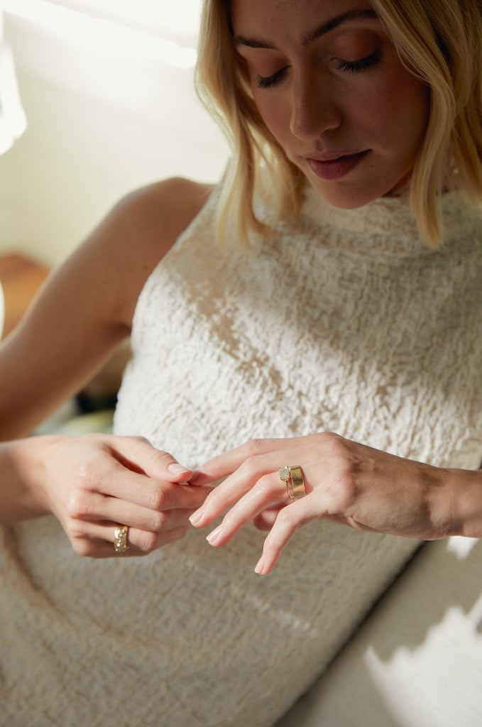 woman wearing gold four prong emerald cut white diamond ring alongside other gold rings