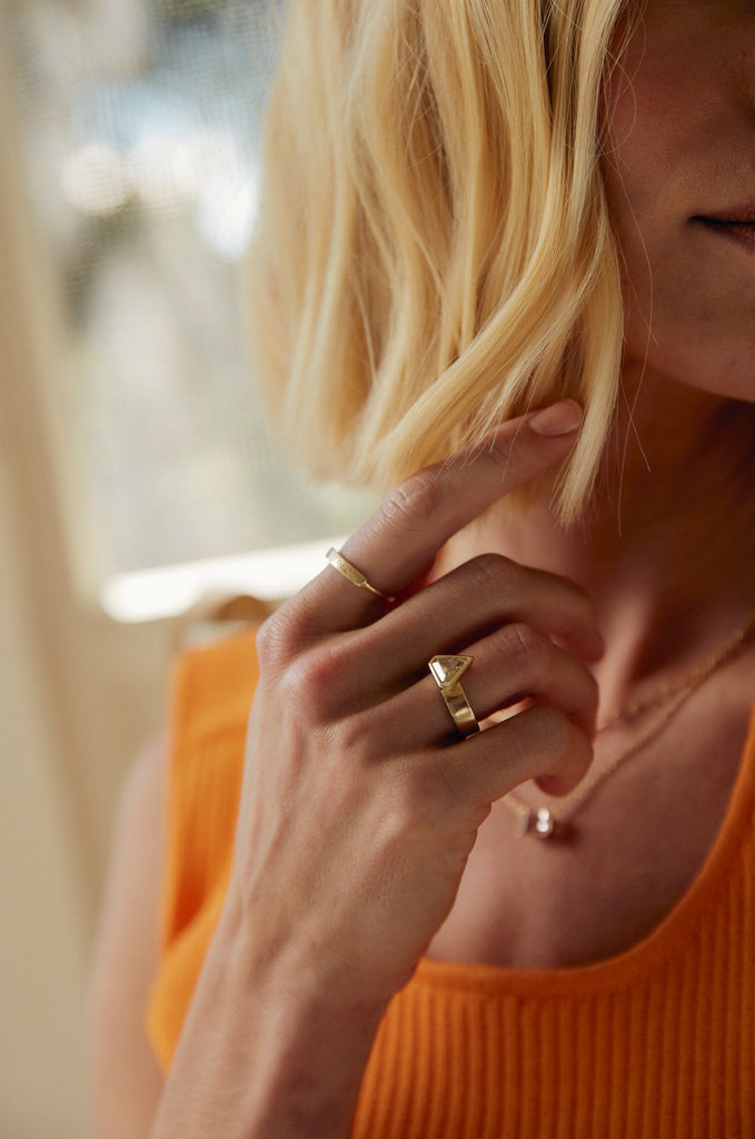 gold band with bezel set shield shaped yellow brown diamond on woman's hand alongside other gold jewelry