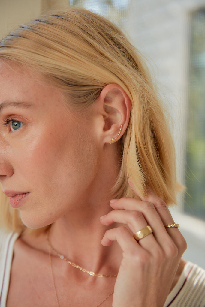 woman wearing gold climber earring with round bezel set white diamond stud alongside other gold jewelry