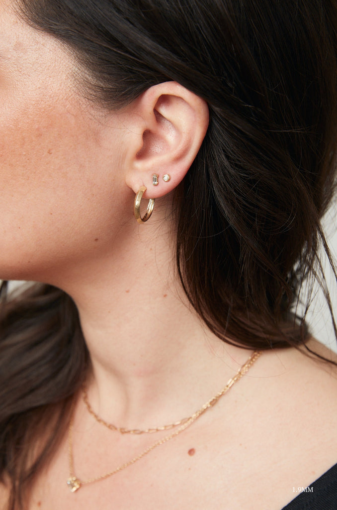 close up of woman wearing free form gold stud earrings with round white diamond alongside other gold earrings