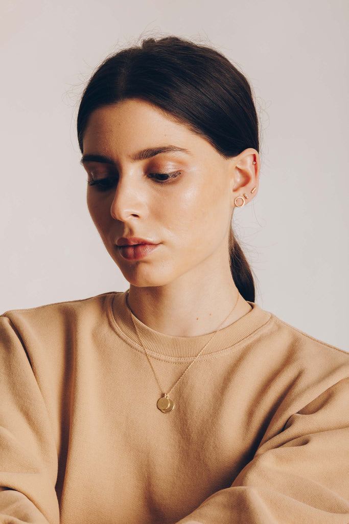 woman wearing gold necklace with two discs alongside other gold jewelry