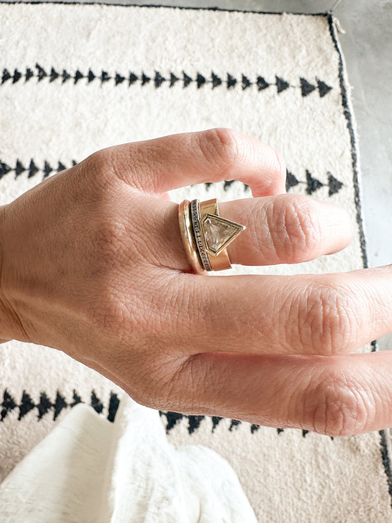 gold band with bezel set shield shaped yellow brown diamond on hand alongside other rings