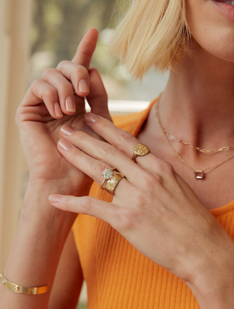 woman wearing four prong gold ring with round white diamond alongside other gold jewelry