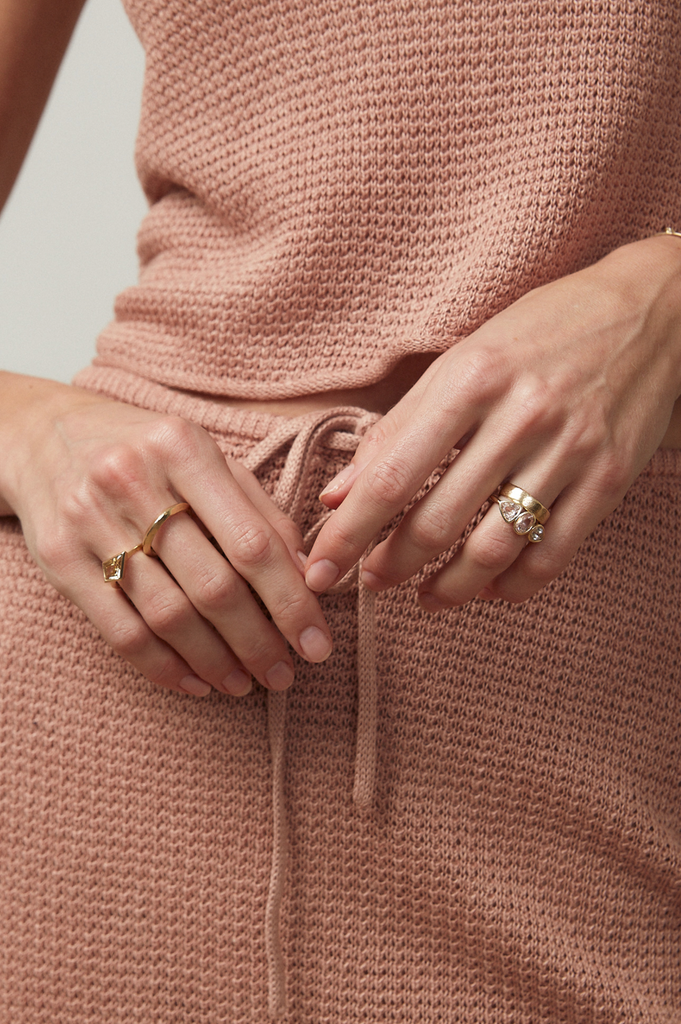 close up of hands wearing gold ring with three bezel set morganites alongside other gold rings