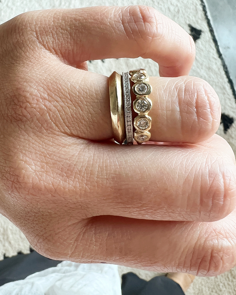 close up of hand wearing knife edge cut gold band alongside other rings