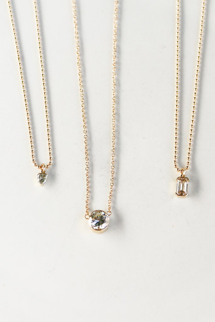 close up of gold ball chain necklace with partial bezel set emerald cut diamond alongside other diamond necklaces