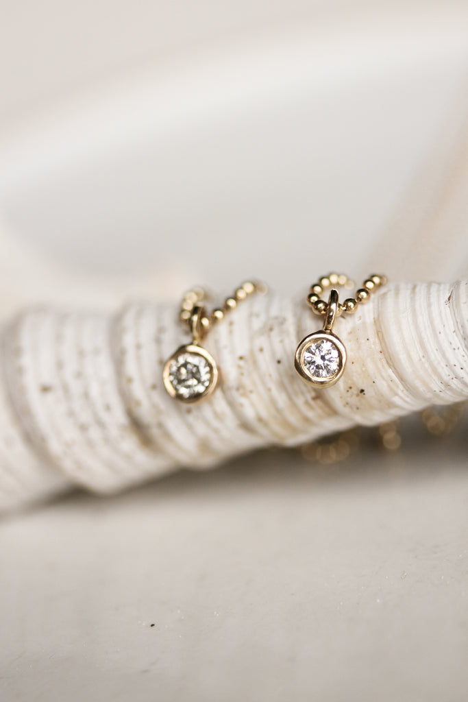 close up of two bezel set round diamond ring on ball chain necklaces