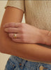close up of woman's hand wearing gold band with emerald cut champagne diamond and two round white diamonds alongside other gold jewelry