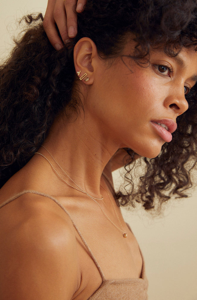 woman wearing emerald cut champagne diamond studs alongside other gold jewelry