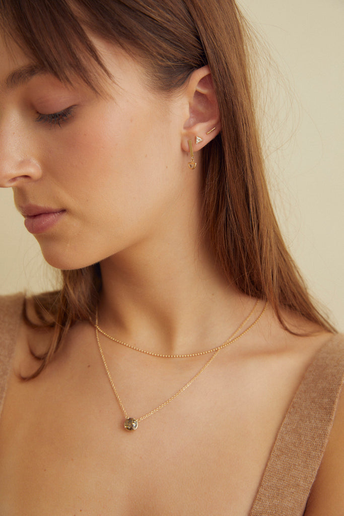 close up of woman wearing gold necklace with round mocha diamond alongside other gold jewelry