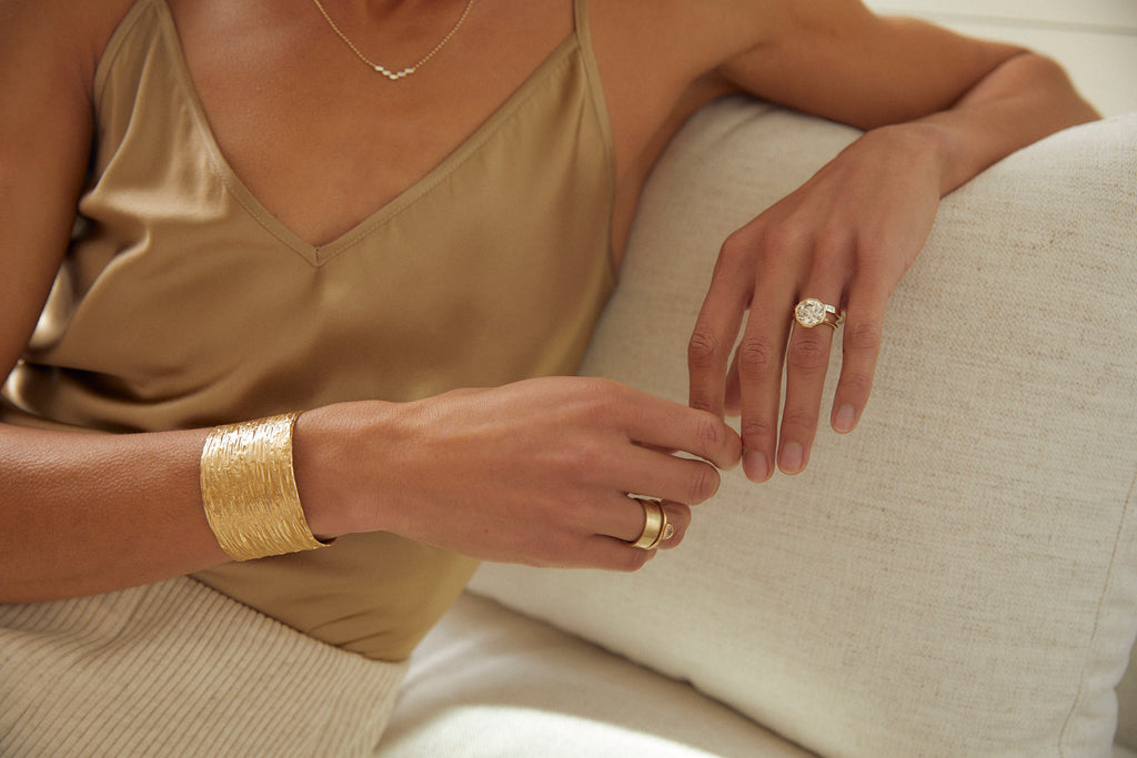 close up of woman wearing gold ring with decagon bezel set round brilliant diamond alongside other gold jewelry