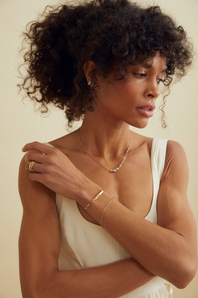 woman wearing gold cable chain necklace with three bezel set round diamonds alongside other gold jewelry