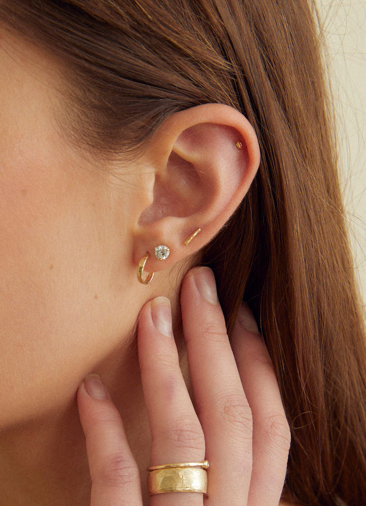 close up of woman wearing gold straight cut hoop earring alongside other gold earrings