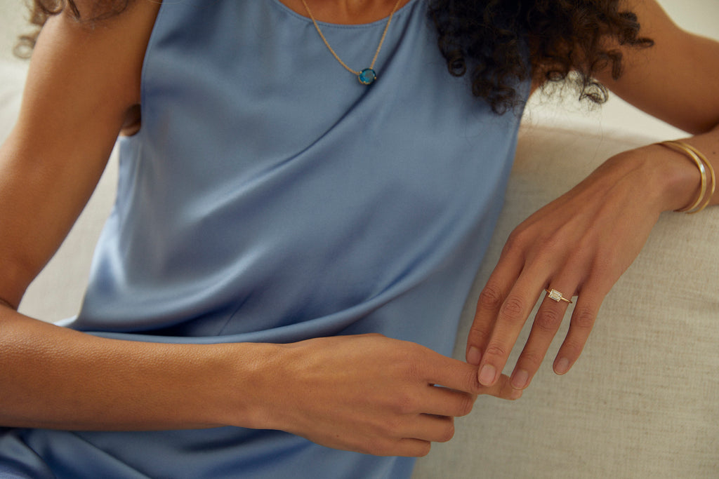 close up of woman wearing gold four prong emerald cut white diamond ring