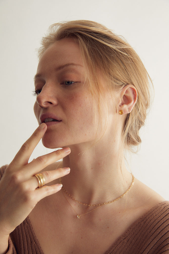 woman wearing round citrine stud with gold three prong martini setting alongside other gold jewelry