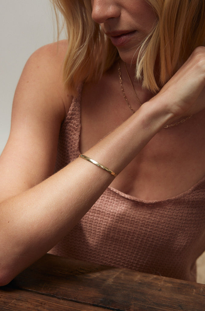 close up of woman wearing gold cuff with rounded edges alongside gold necklaces