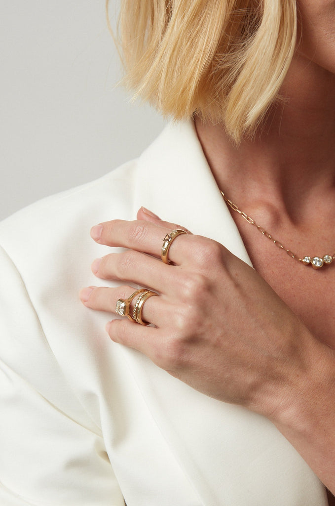 woman wearing gold band with emerald cut champagne diamond and two round white diamonds alongside other gold jewelry