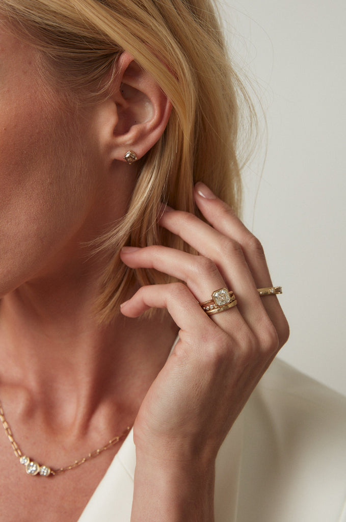 close up of woman wearing gold ring with bezel set asscher cut white diamond alongside other gold jewelry