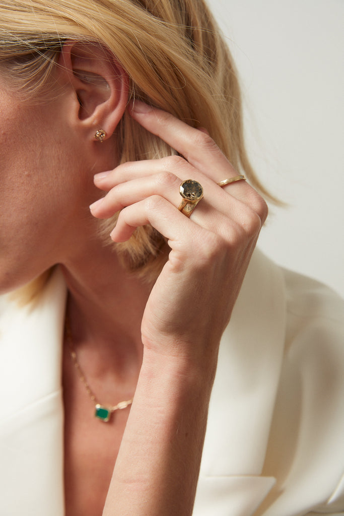 woman wearing gold ring with decagon bezel set round mocha diamond alongside other gold jewelry
