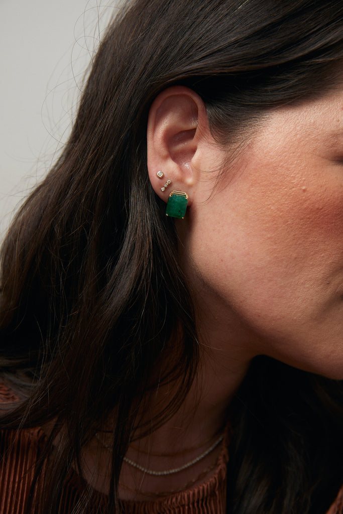 woman wearing gold earring with three bezel set round white diamonds alongside other gold earrings