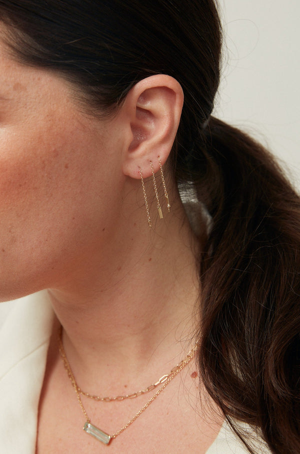 woman wearing gold drop earring with baguette diamond on end alongside other drop earrings