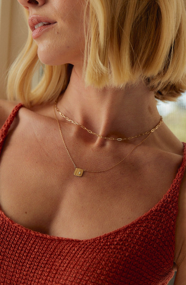 woman wearing gold necklace with gold square design containing baguette white diamond alongside cable chain