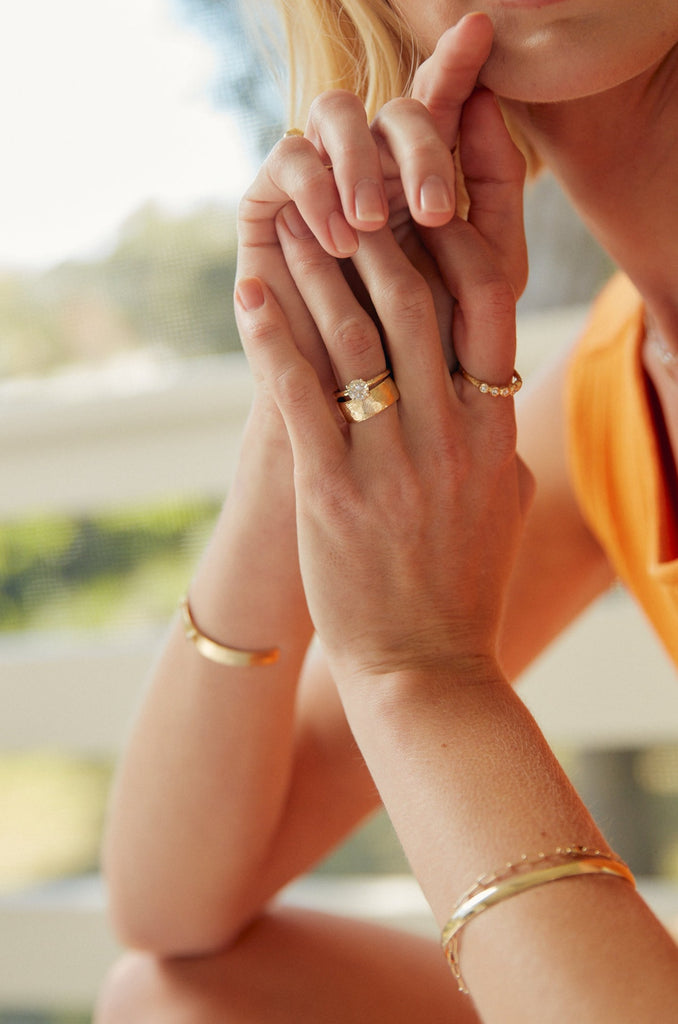 close up of woman wearing gold textured cigar band alongside other gold jewelry