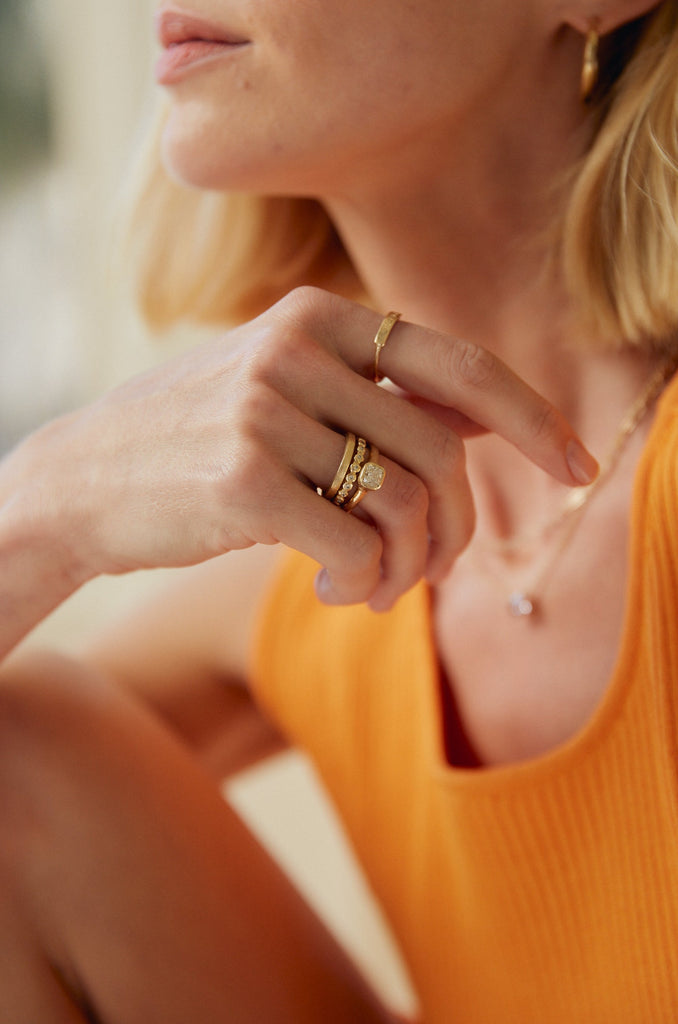woman wearing thin gold band with straight sides alongside other gold jewelry