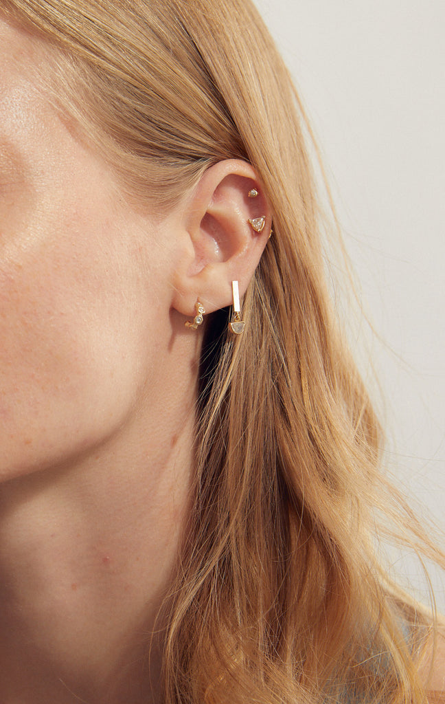 woman wearing free form gold stud earrings with round white diamond alongside other gold earrings