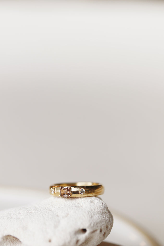 close up of gold band with emerald cut champagne diamond and two round white diamonds