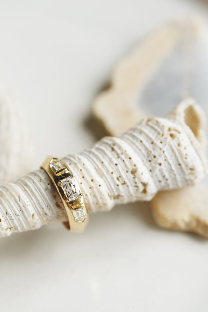close up of gold knife edge band with two bullet cut white side diamonds and center round-cornered rectangular white ocean diamond