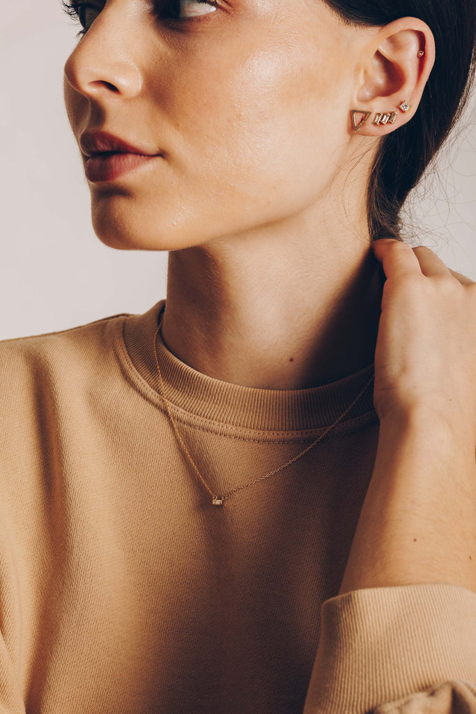 woman wearing gold necklace with white diamond baguette alongside other gold jewelry