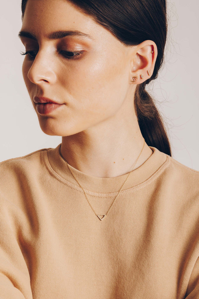 woman wearing gold necklace with gold triangle alongside other gold jewelry