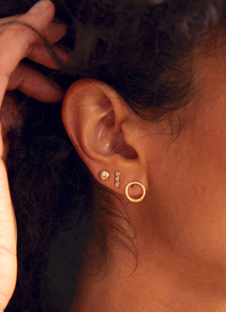 woman wearing gold earring with three bezel set round white diamonds alongside other gold earrings