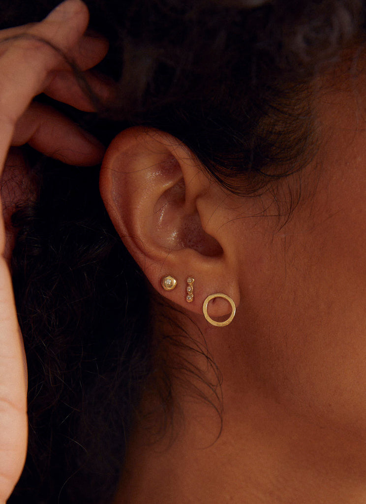 close up of woman wearing gold bezel set round white diamond stud alongside other gold earrings