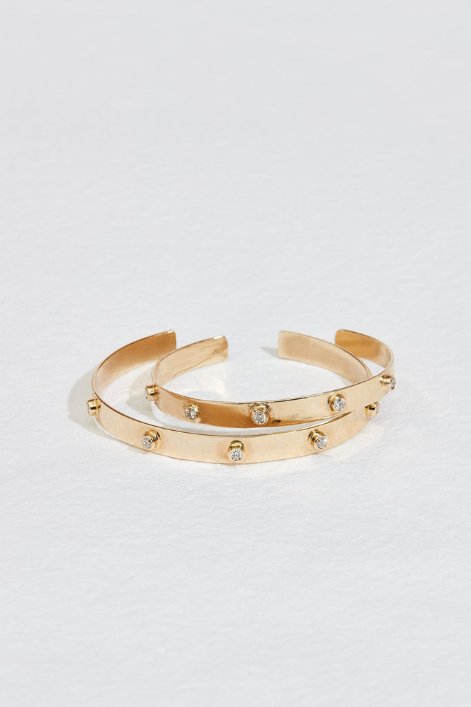 close up of two gold cuff bracelets studded with round diamonds