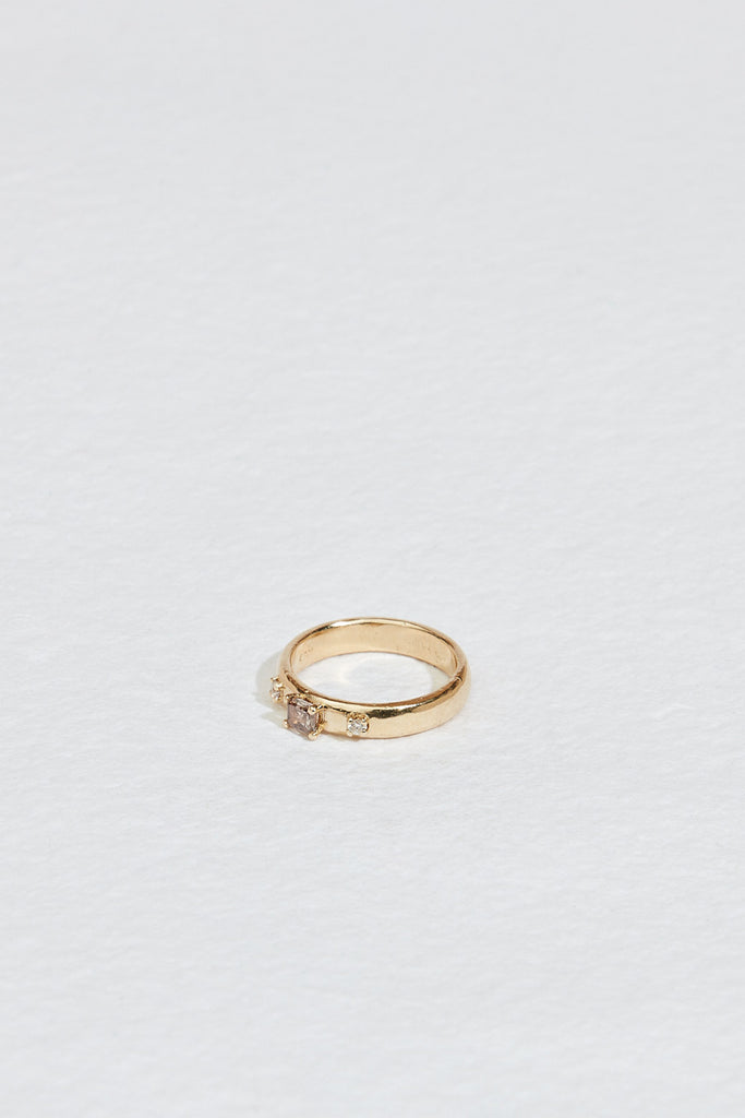 side view of gold band with emerald cut champagne diamond and two round white diamonds