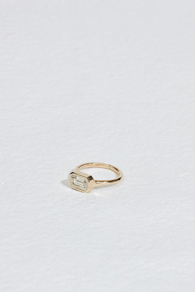 side view of gold ring with bezel set emerald cut white diamond