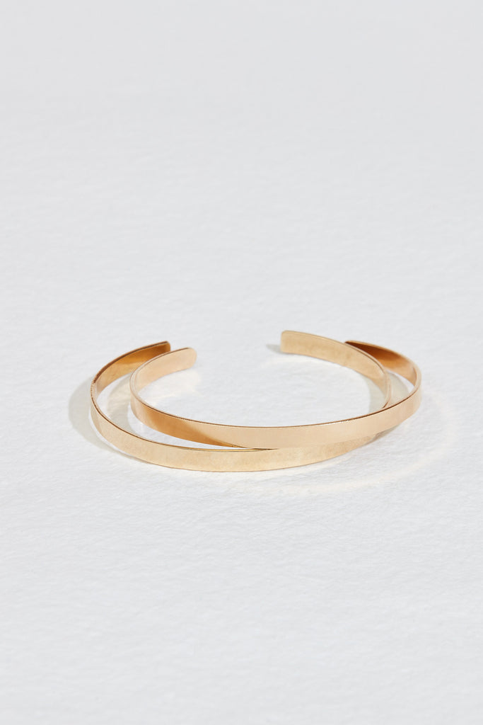 close up of two gold flat cuff bracelets