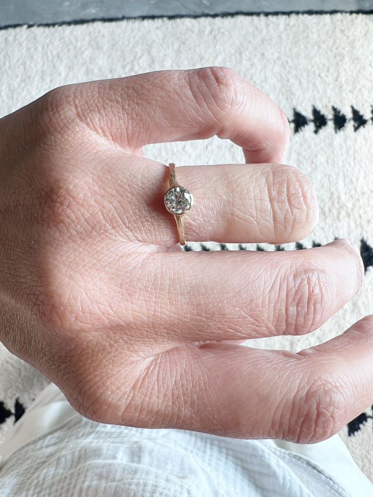 close up of hand wearing gold ring with bezel set round white diamond