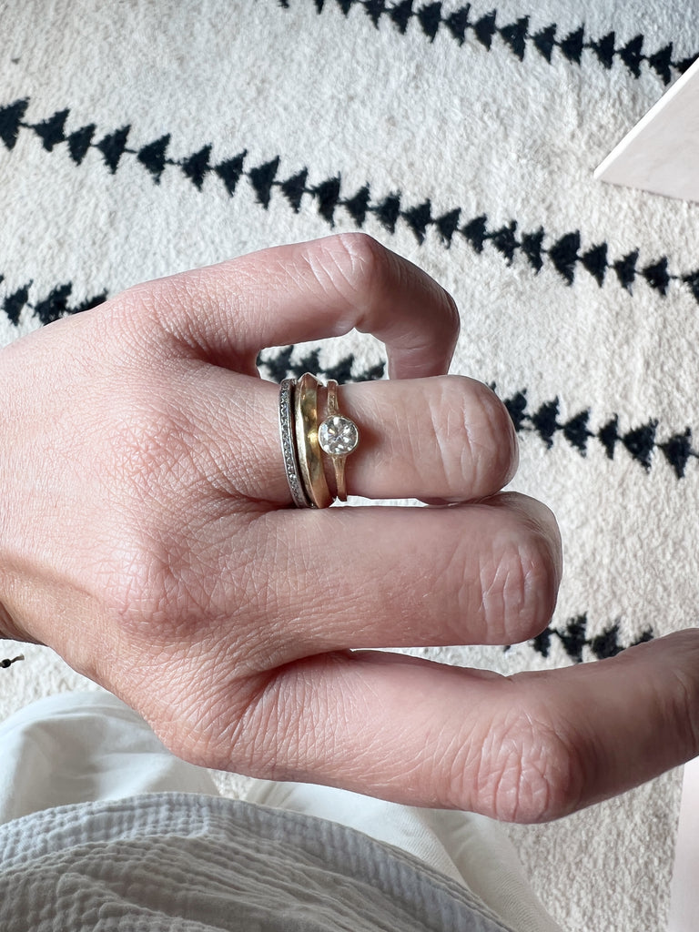 close up of hand wearing gold ring with bezel set round white diamond