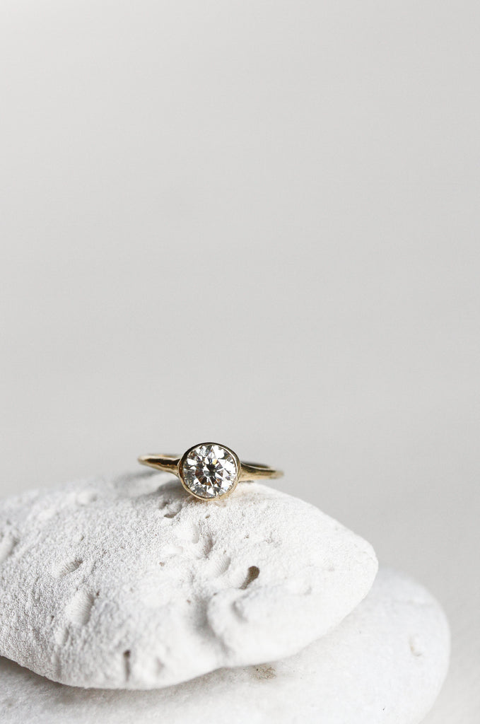 close up of gold ring with bezel set round white diamond