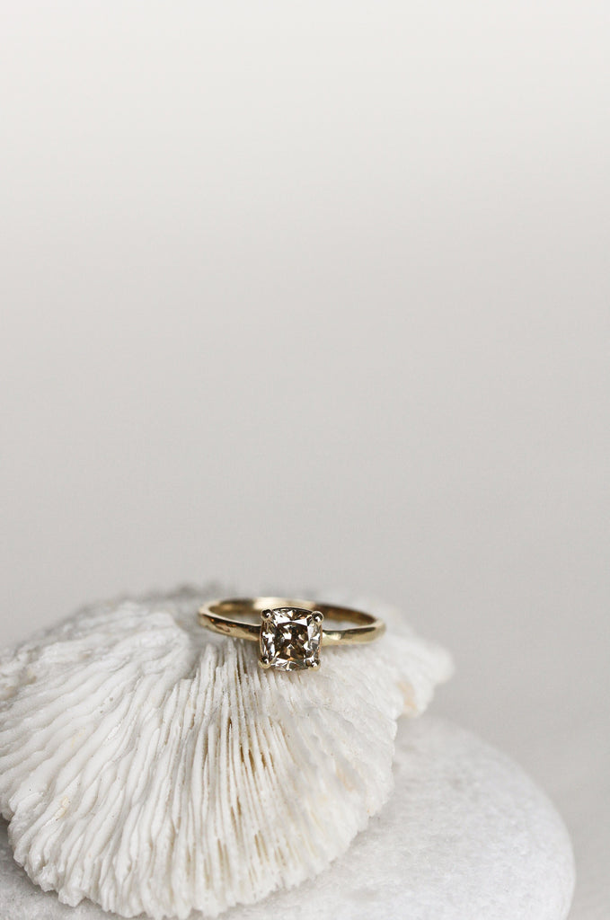close up of four prong gold ring with cushion cut light champagne diamond