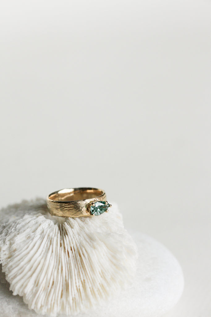 close up of wide gold band with blue green pear diamond