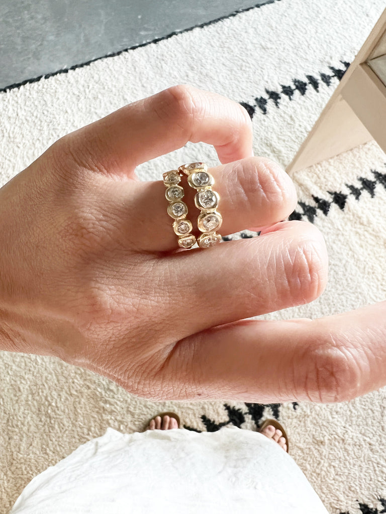 close up of hand wearing two gold band with six bezel set round diamonds