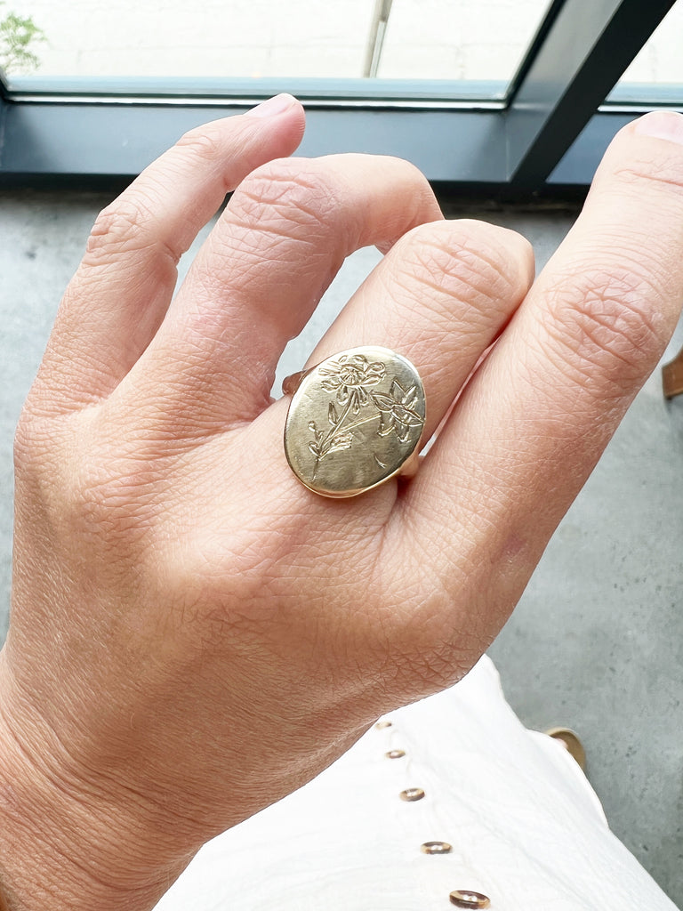 close up of gold signet ring with engraved flowers on hand