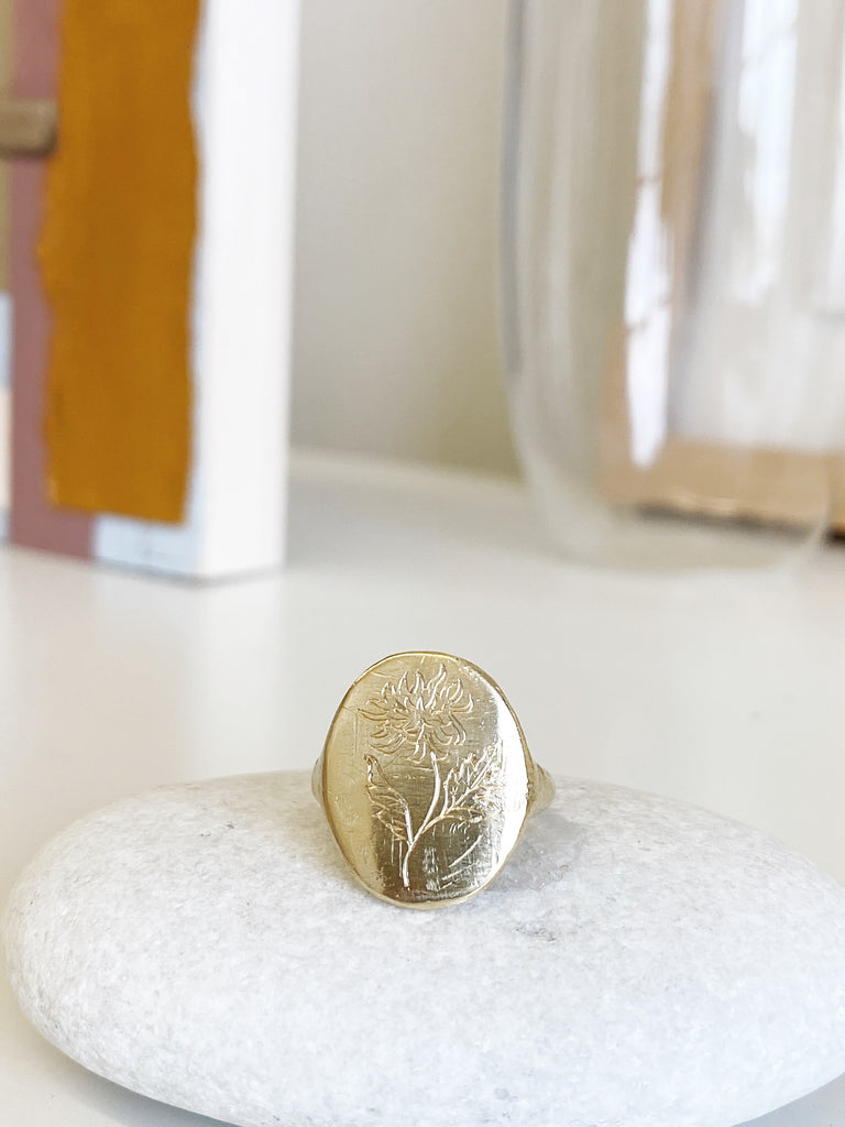close up of gold signet ring with engraved flowers on rock